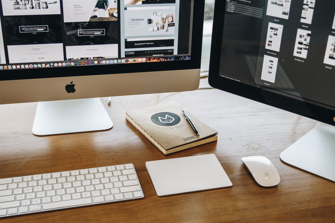 who-we-are A minimalist desk setup featuring dual monitors, keyboard, mouse, and notebook for productivity.